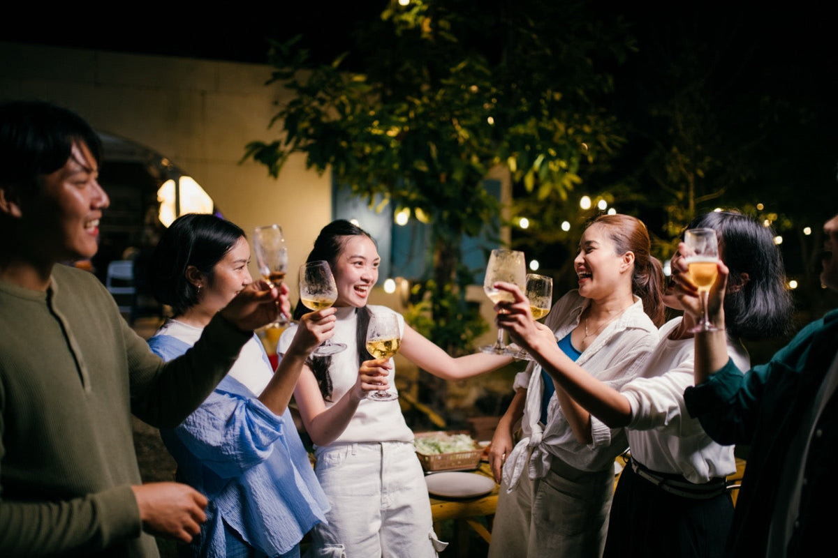 Group of friends raising drinks at an outdoor evening gathering, with the middle woman showing facial flushing as a visible sign of Alcohol Intolerance