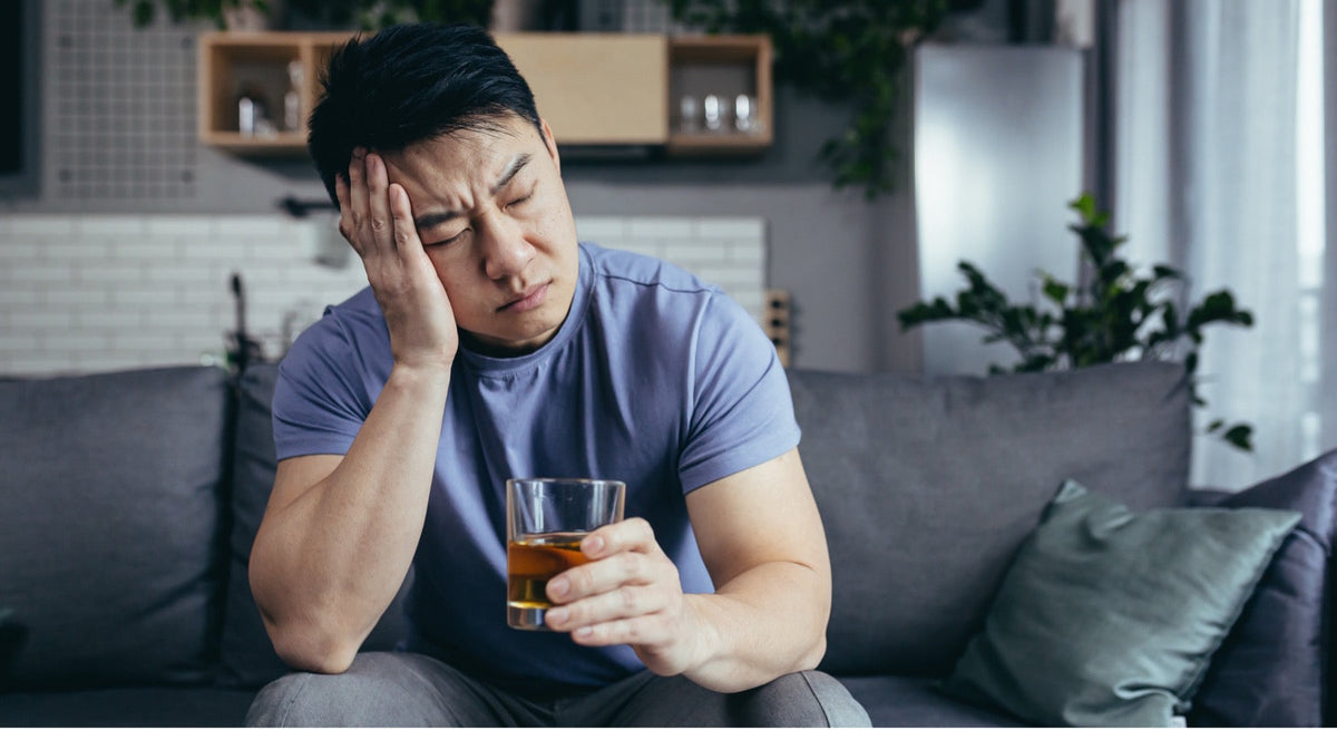 Asian man holding a drink and experiencing a headache while dealing with hangover symptoms